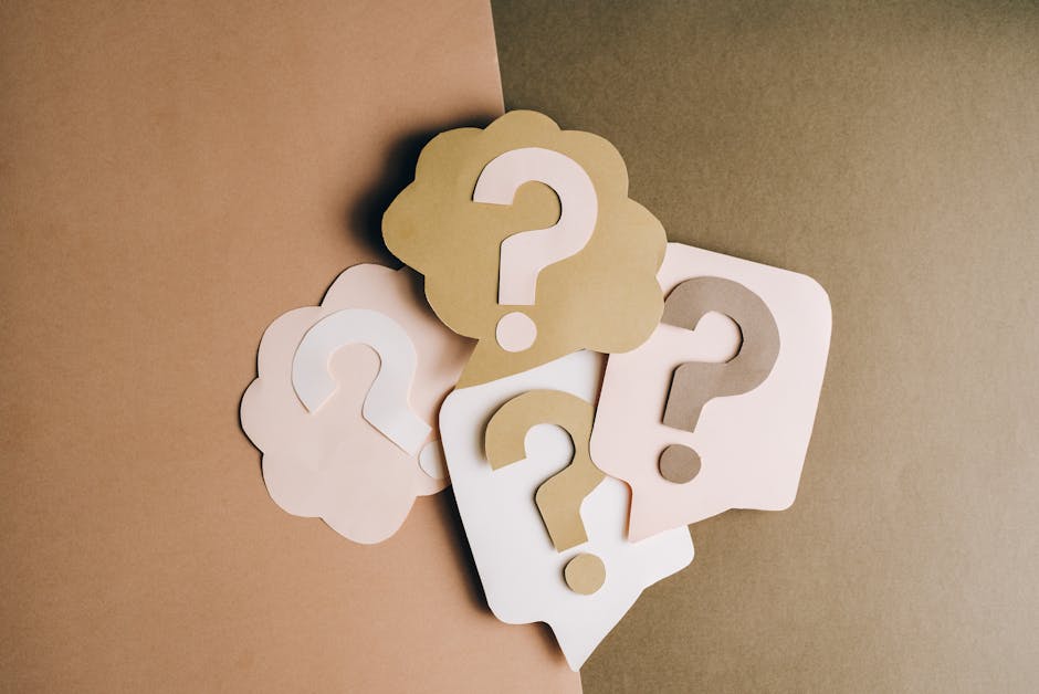 The image displays a collection of five paper cutouts of speech bubbles with question marks inside them. These speech bubbles are made of thick paper or cardstock, with smooth edges and a matte finish